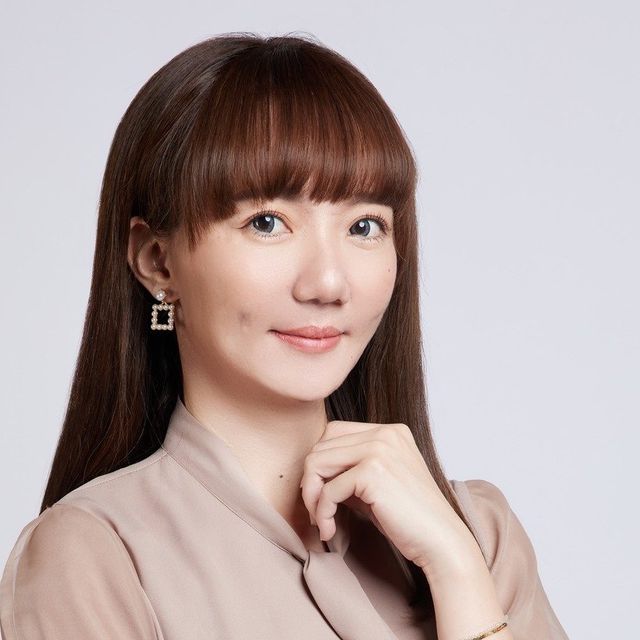 黛比（曾郁蓉）的照片，米色上衣、淺灰背景，單手輕觸下巴微笑